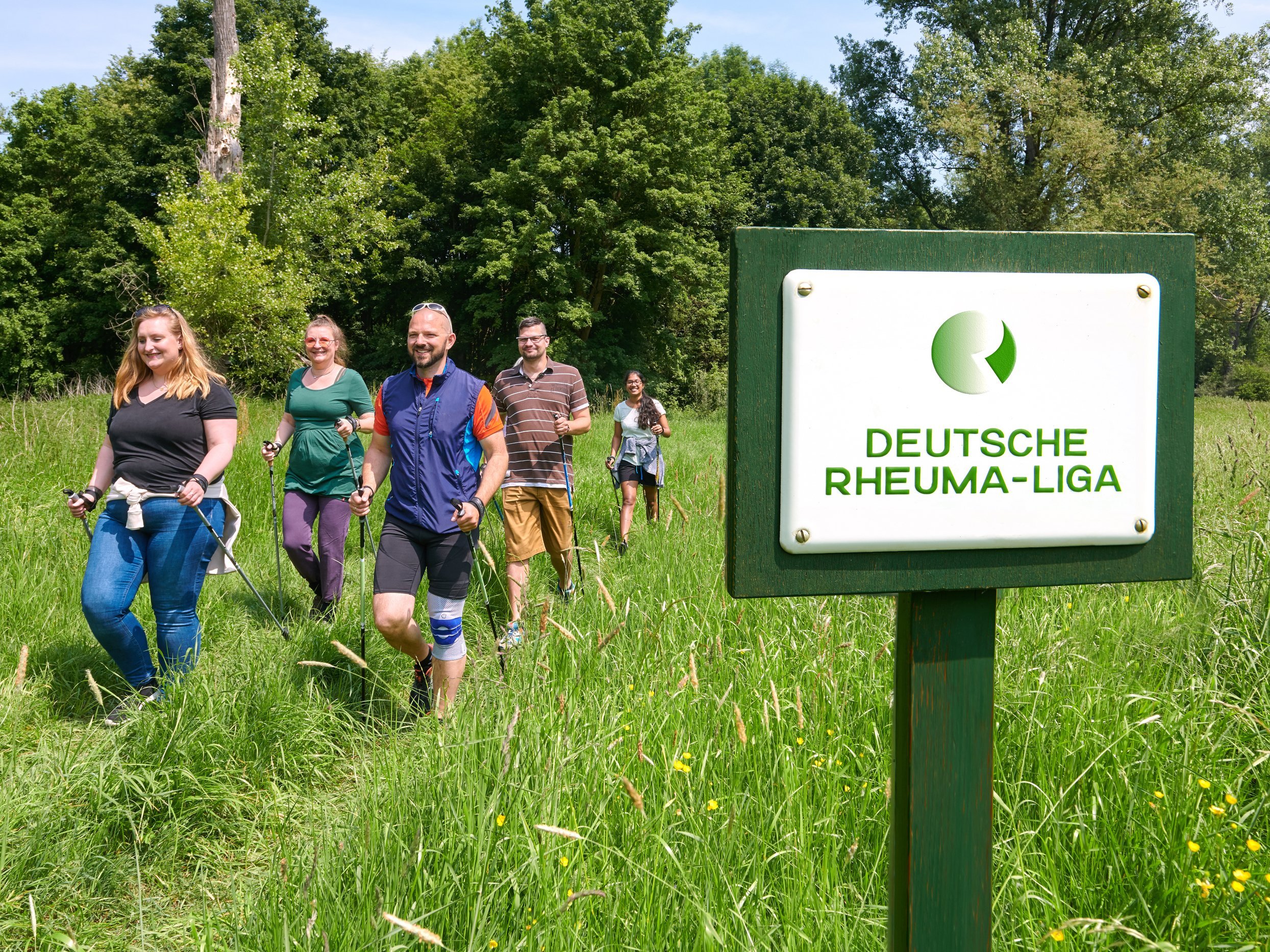 Gruppe von Menschen beim Nordic Walken, im Vordergrund Schild mit der Aufschrift "Deutsche Rheumaliga Bundesverband"